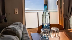 Una habitación con un sofá, una mesa de madera con una botella y vasos, y un ventanal con vistas al cielo.
