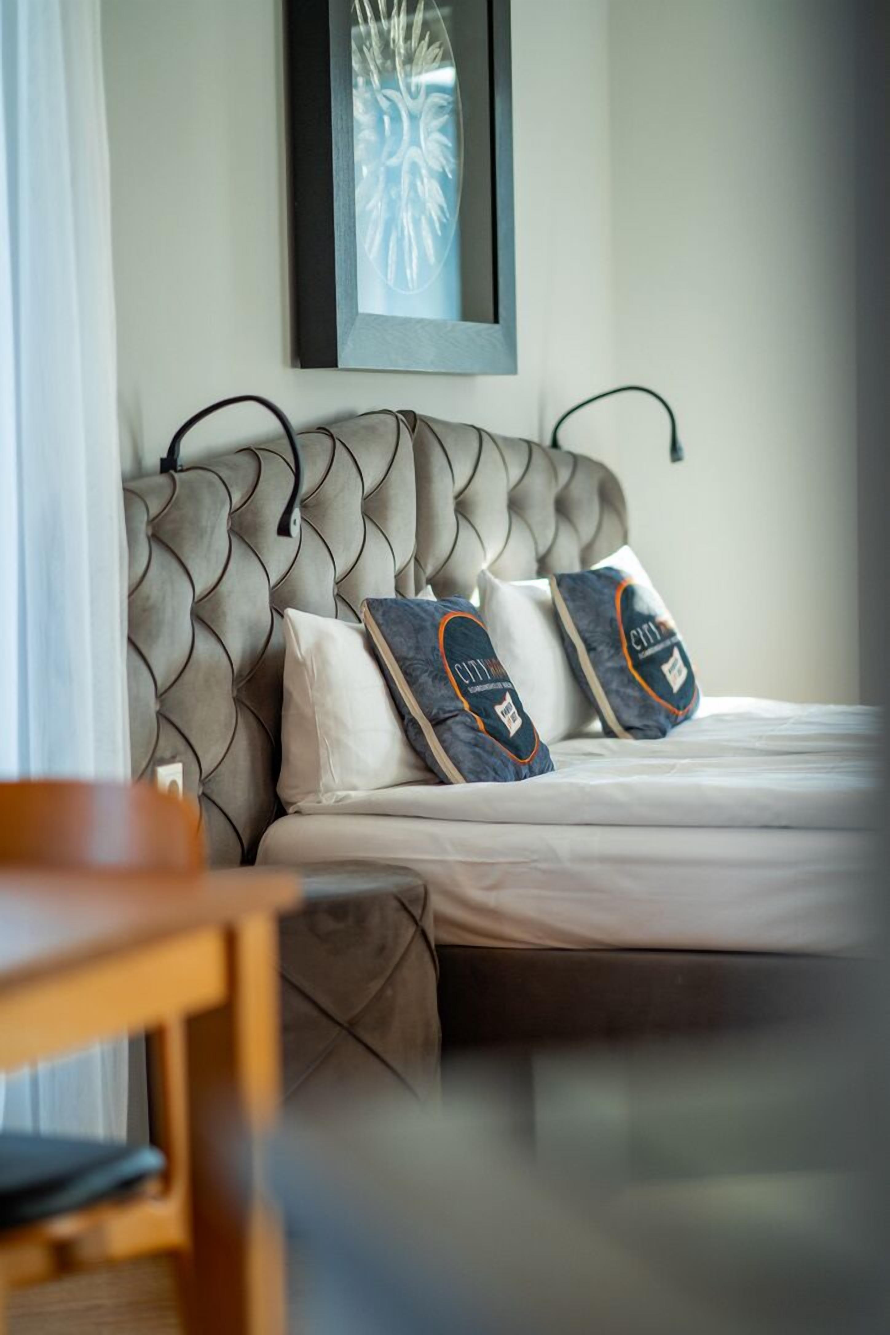 A bed with a tufted headboard, two pillows with a logo, and a framed artwork above.