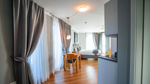 Habitación de hotel moderna con piso de madera, zona de comedor con mesa y sillas, y cama con mesita de noche.