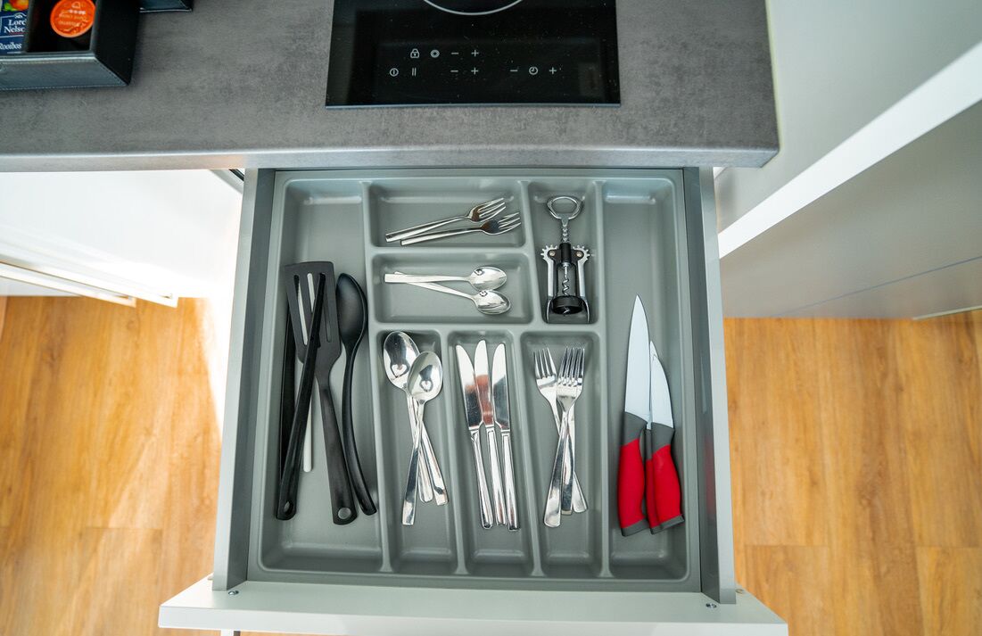 Eine Schublade mit ordentlich sortierten Küchenutensilien, darunter Löffel, Gabeln, Messer und ein Flaschenöffner.