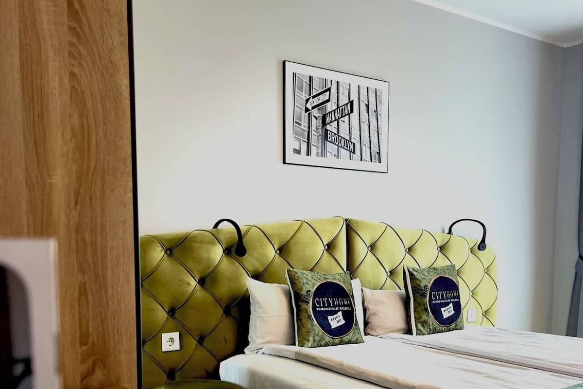 A neatly arranged bedroom with a green tufted headboard, a framed city street sign, and two decorative pillows.