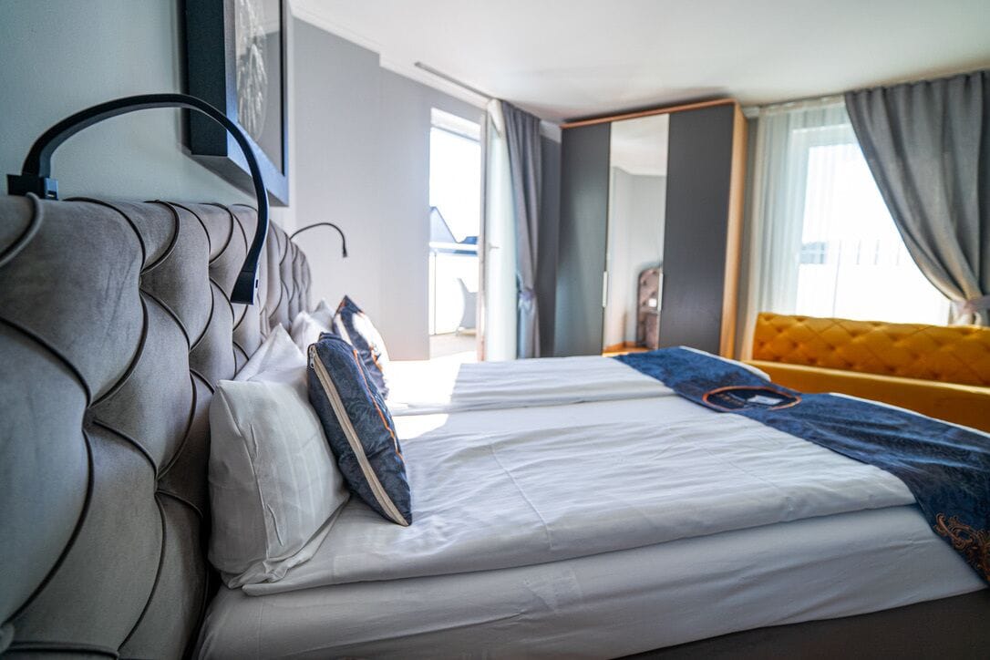 Habitación de hotel moderna con una cama grande, cabecero, sofá y vistas al exterior.
