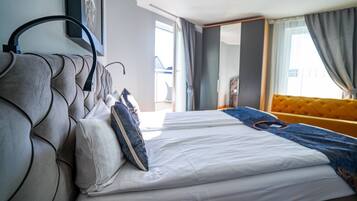 Habitación de hotel moderna con una cama grande, cabecero, sofá y vistas al exterior.