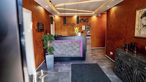 Un área de recepción con una pared de madera, un mostrador de recepción con detalles rosas y una consola negra.