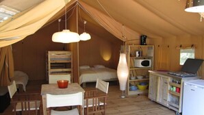 Une tente confortable équipée d’un lit, d’une table avec des chaises, d’une lampe, d’un four à micro-ondes et d’un réfrigérateur.