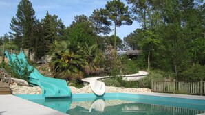 Une piscine avec un toboggan et une petite cascade, entourée d’arbres et d’une clôture en bois.