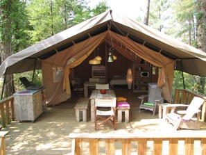 A tent with a wooden deck, a dining table, chairs, and a hanging light fixture. - Camping la Tuque (Belaye)