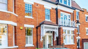 A two-story brick house with a balcony, white-framed windows, and a front door with a decorative archway. - Stunning studio with funky decor in Highgate village - perfect for couples! (London)