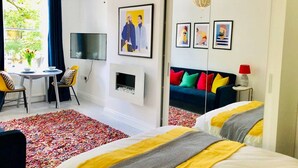 A modern hotel room with a sofa, a TV, a dining area with a table and chairs, and a colorful rug. - Stunning studio with funky decor in Highgate village - perfect for couples! (London)