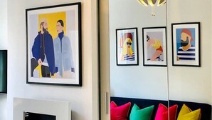 A modern living room with a blue sofa, colorful cushions, and framed artwork on the wall. - Stunning studio with funky decor in Highgate village - perfect for couples! (London)
