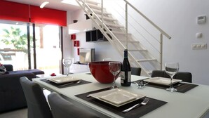 A modern dining area with a white table set for four, red bowl centerpiece, wine bottle, and glasses. A staircase is visible in the background. - Casa Alexandra 4-person penthouse on the seafront in Mar de Pulpi. (Pulpí)