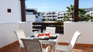 A terrace with a table set for two, overlooking a residential area with white buildings and palm trees. - Casa Alexandra 4-person penthouse on the seafront in Mar de Pulpi. (Pulpí)