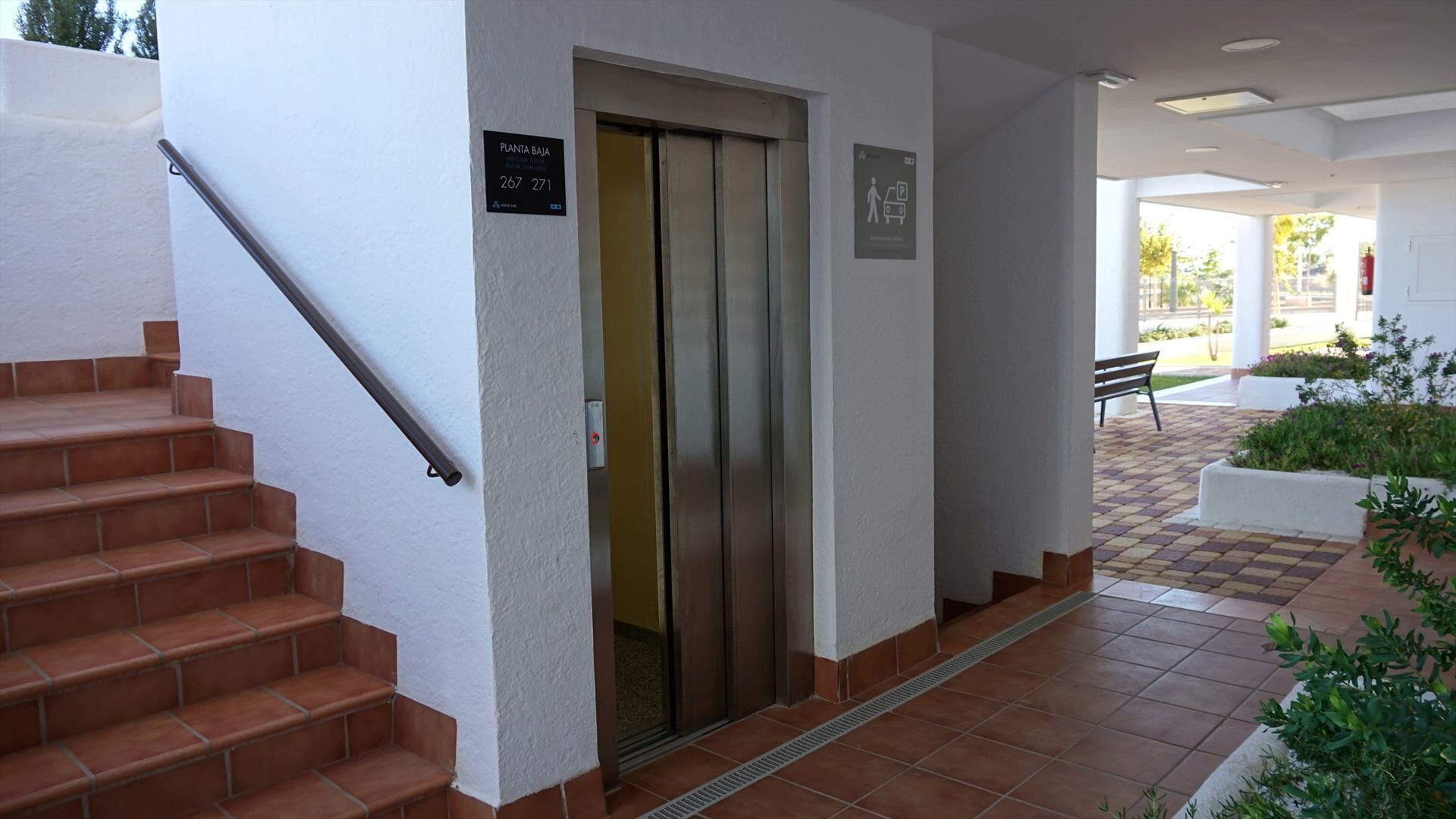 A building entrance with a staircase, an elevator, and a sign indicating the location.