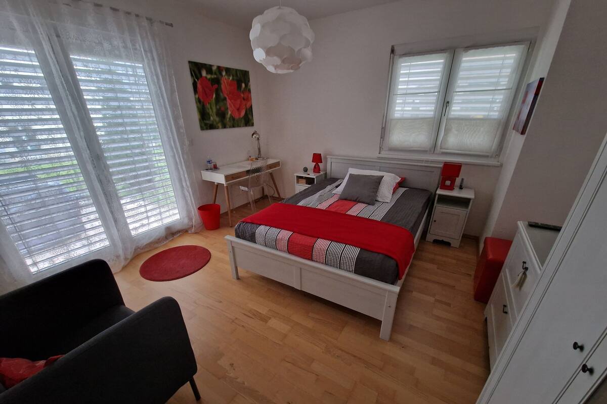 A bedroom with a bed, a desk, a chair, a wardrobe, and a window with blinds.
