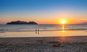 Ein Strand bei Sonnenuntergang, ruhiges Meer und entfernte Landformen.