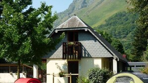 A mountain lodge with a balcony, a red tent, and a green tent in the foreground. - Camping L'Arrayade (Ger)