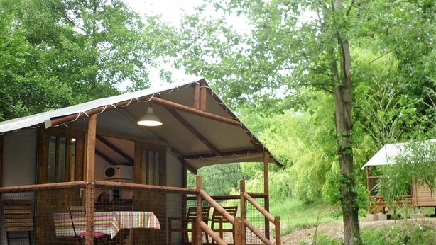 A rustic wooden cabin with a covered porch and a small table with chairs. - Camping L'Arrayade (Ger)