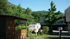 A residential area with a camper parked in front of a house, surrounded by greenery and hills. - Camping L'Arrayade (Ger)