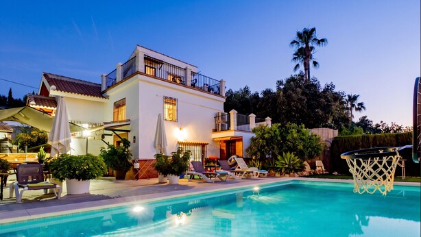 Una casa moderna de dos pisos con piscina, mobiliario de exterior y un aro de baloncesto.