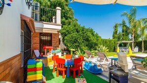 Un patio con piscina, mobiliario exterior y zona de juegos para niños.