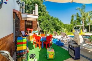 Een terras met een zwembad, buitenmeubels en een kinderspeelplaats.