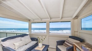A balcony with wicker furniture, a view of the ocean, and a wooden table with decorative items. - Oceanfront Beauty with views from every room (Stinson Beach)
