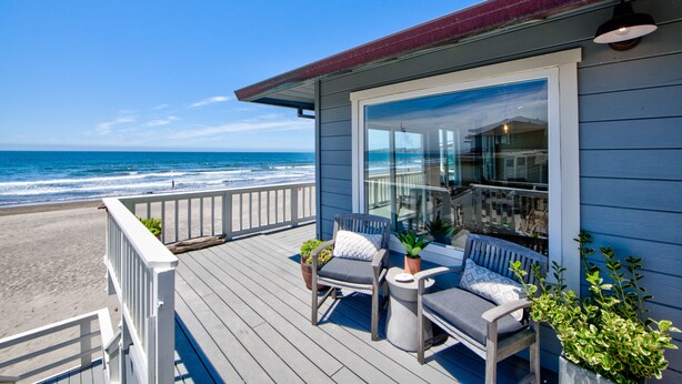 A wooden deck with two chairs and a table, overlooking a beach and ocean. - Oceanfront Beauty with views from every room (Stinson Beach)