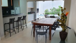 Ein Essbereich mit Holztisch und Stühlen, eine Küche im Hintergrund und ein Blick auf einen Garten durch eine offene Tür.
