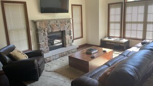 A living room with a stone fireplace, leather sofa, and a flat-screen TV mounted above the fireplace.