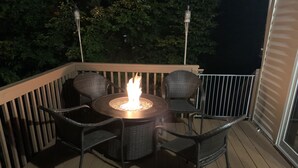 A deck with a round table and four chairs, a fire pit in the center, and a railing.