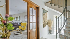 A spacious living room with a sofa, a yellow armchair, and a coffee table. A wooden door leads to a staircase with a metal railing. - Alcam Can Macia (Corbera De Llobregat)