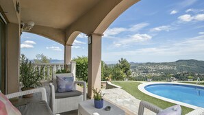 A covered outdoor area with wicker furniture, a pool, and a view of a town and hills. - Alcam Can Macia (Corbera De Llobregat)