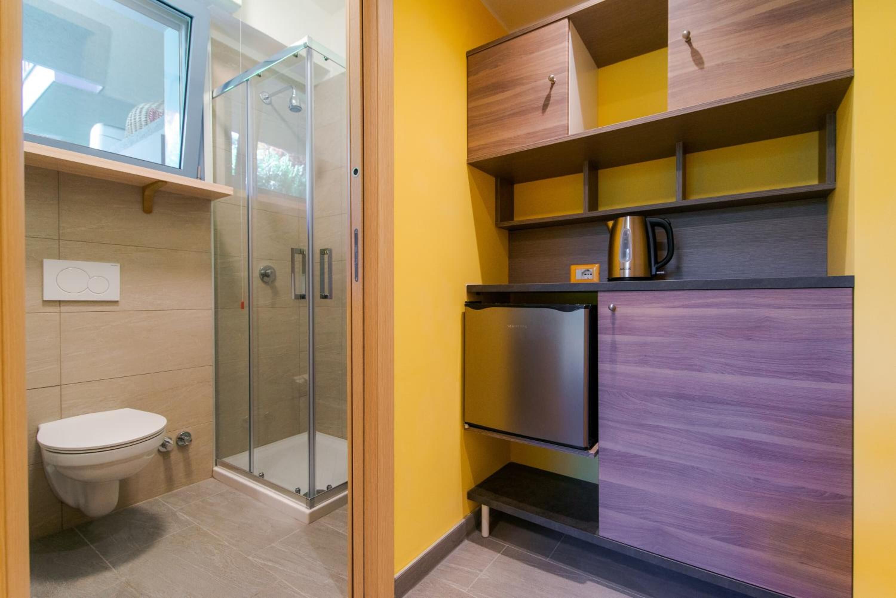 Ein kleines Badezimmer mit Duschkabine aus Glas, Toilette und integriertem Schrank mit Wasserkocher.