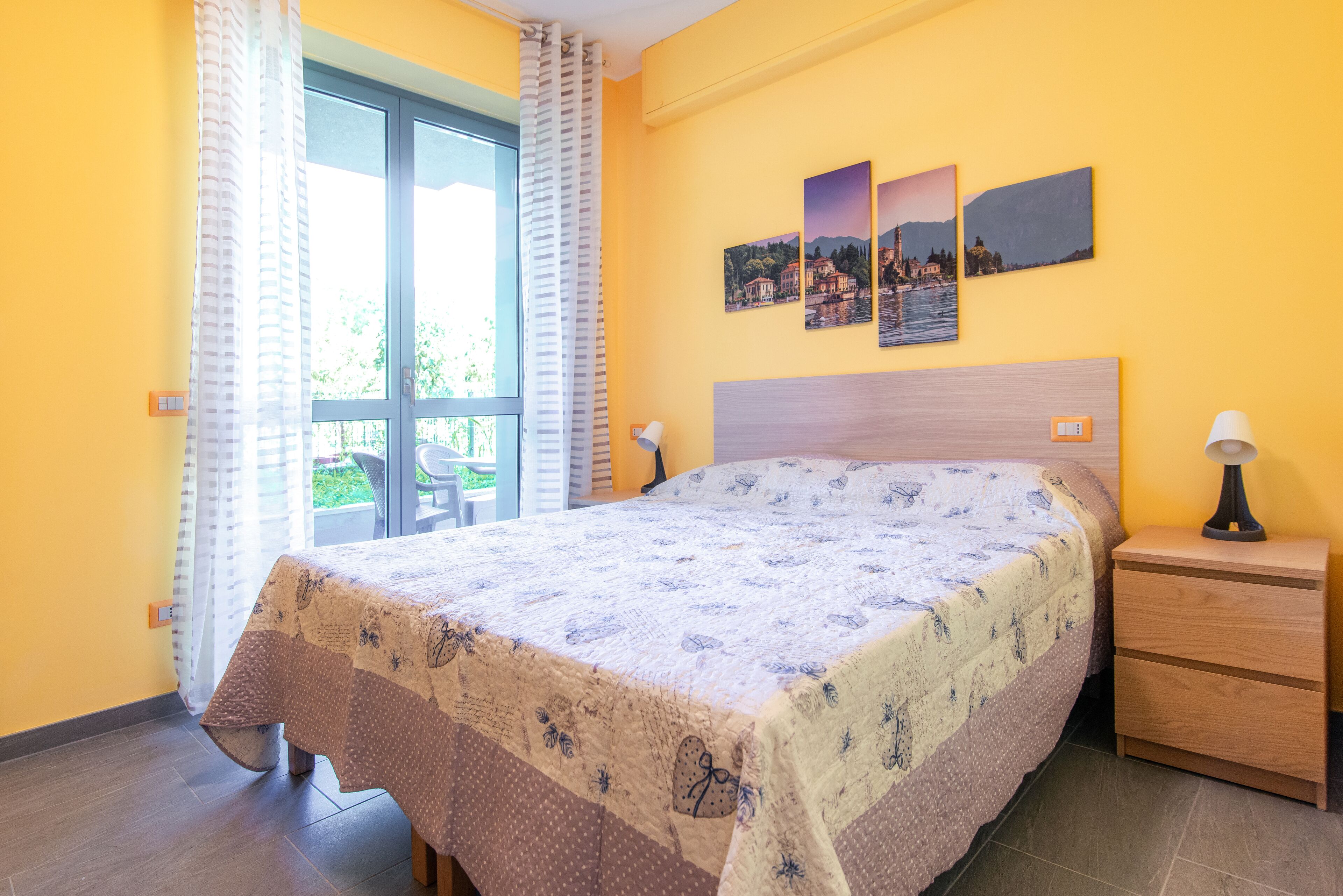 Ein Schlafzimmer mit einem Bett, einem Nachttisch, einer Lampe, einem Fenster mit Vorhängen und drei Wandbildern.