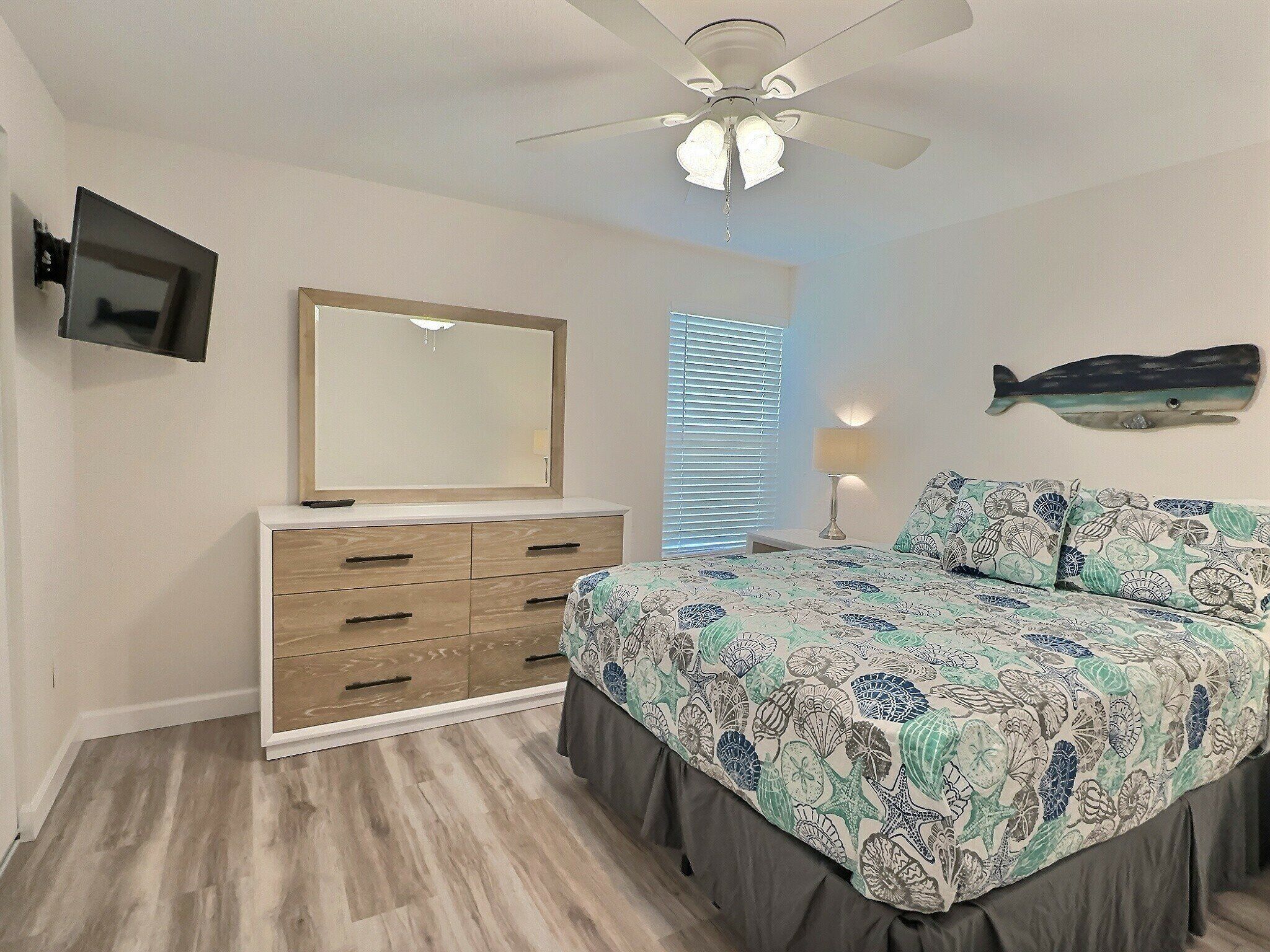 A bedroom with a bed, dresser, ceiling fan, TV, and a wall-mounted fish decoration.