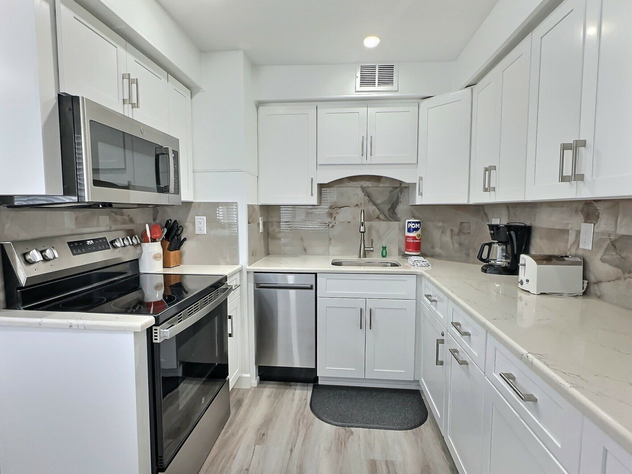 A compact kitchen with white cabinets, a microwave, a stove, a dishwasher, and a coffee maker.