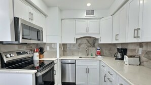 A compact kitchen with white cabinets, a microwave, a stove, a dishwasher, and a coffee maker. - Beachside Vacation Rental Condo on Siesta Key with Pool Access (Siesta Key)
