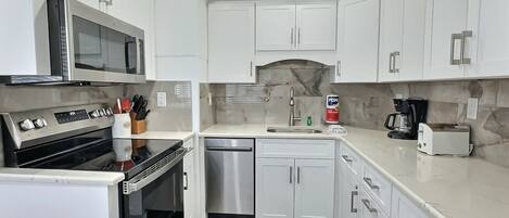 A compact kitchen with white cabinets, a microwave, a stove, a dishwasher, and a coffee maker.