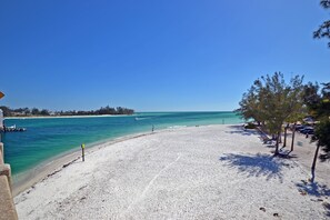 Ein Strand mit klarem türkisblauem Wasser, einem sandigen Ufer und einigen Bäumen.