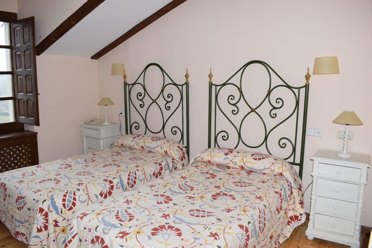A bedroom with a double bed, two bedside tables, a window with wooden shutters, and a white dresser.