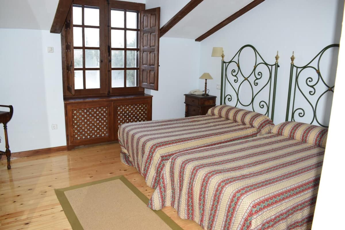 A bedroom with a wooden bed, a window with shutters, a nightstand, and a lamp.