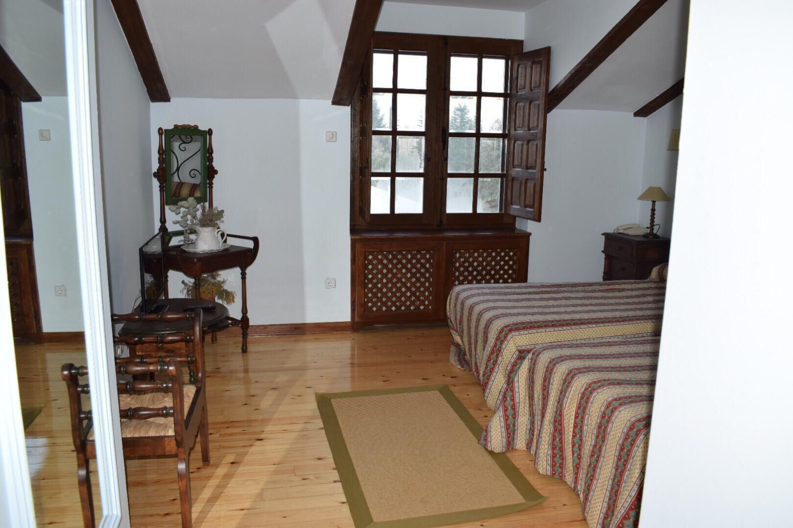 A bedroom with a wooden bed, a desk with a chair, a window, and a door.
