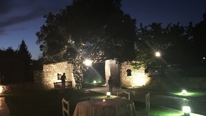 Un área de comedor al aire libre con mesas y sillas, un muro de piedra y un árbol.
