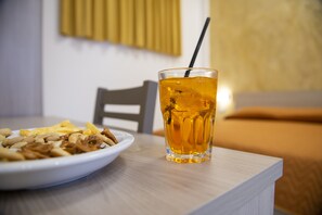 Ein Teller Essen und ein Glas bernsteinfarbenes Getränk auf einem Tisch in einem Zimmer mit Bett und Stuhl.