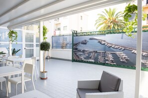Un balcón con vista a un puerto deportivo, muebles blancos y plantas en macetas.