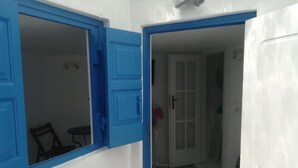 A room with a white and blue door, a tiled floor, and a small table with chairs. - Classy Mykonian Studio - Ornos (Mykonos)