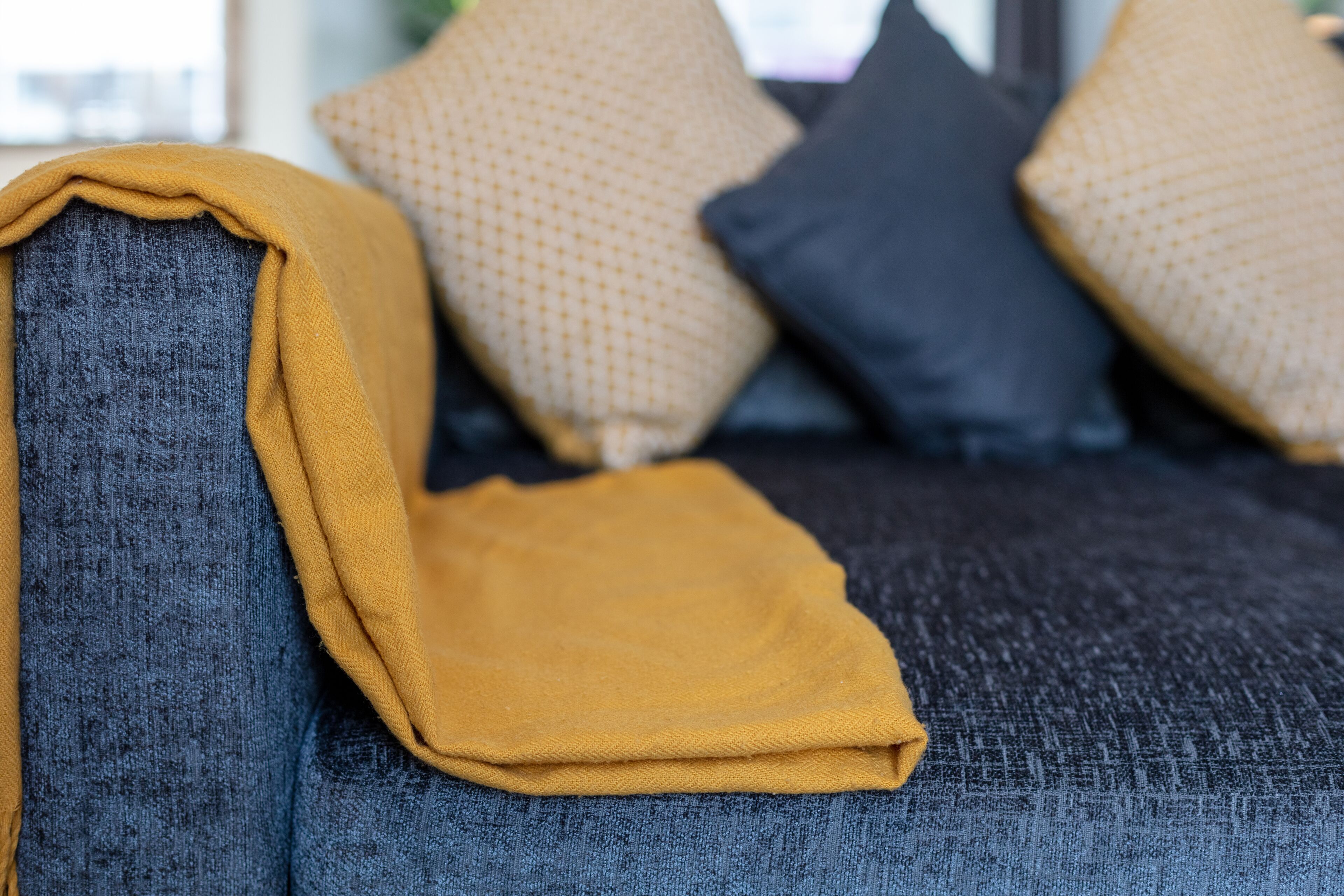 A sofa with a folded blanket and patterned cushions.