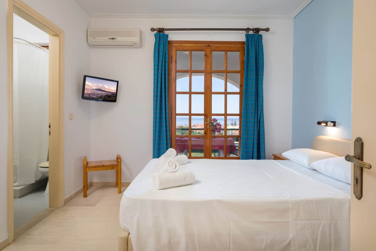 A hotel room with a bed, a television mounted on the wall, and a window with curtains.