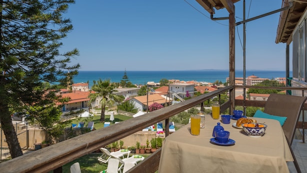 A balcony with a table set for breakfast, overlooking a coastal town and the sea. - Vallia's Apartments (Zakynthos)
