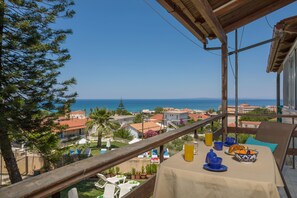 Ein Balkon mit Frühstückstisch, mit Blick auf eine Küstenstadt und das Meer.